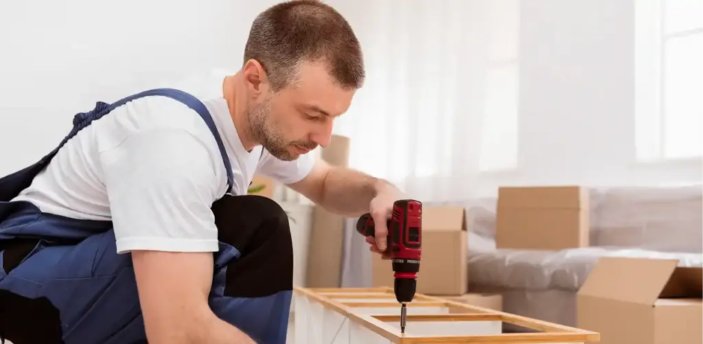 Man in een blauwe overall monteert een plank op de vloer in de kamer.